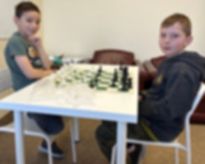 Desk with chess board and children playing chess at Flying Minds education centre chess club