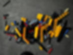 Pile of colorful LEGO Technic pieces, mostly yellow and black, scattered on a gray carpet. Bright hues and varied shapes visible.