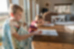 Two kids doing homework sitting by the dining table.